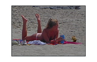 girl lying on the beach on her belly with feet up looking at a chipmunk
